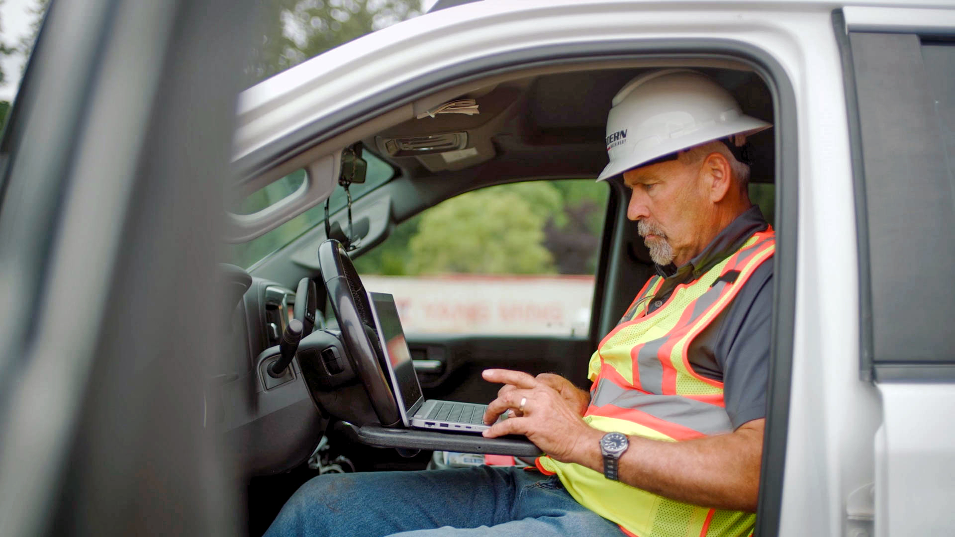 Worker using a notebook computer in the cab of a pickup at a job site.