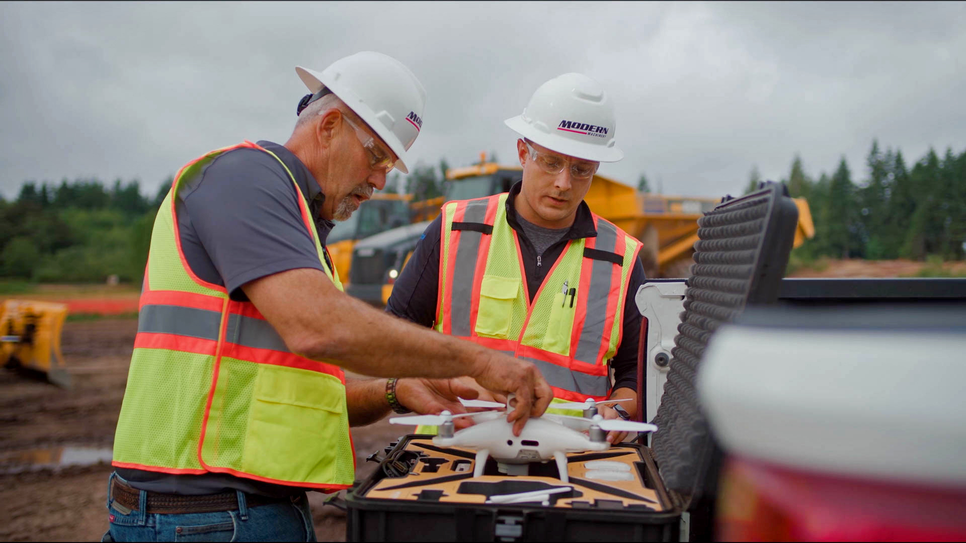Two workers removing a drone from its case at a job site.